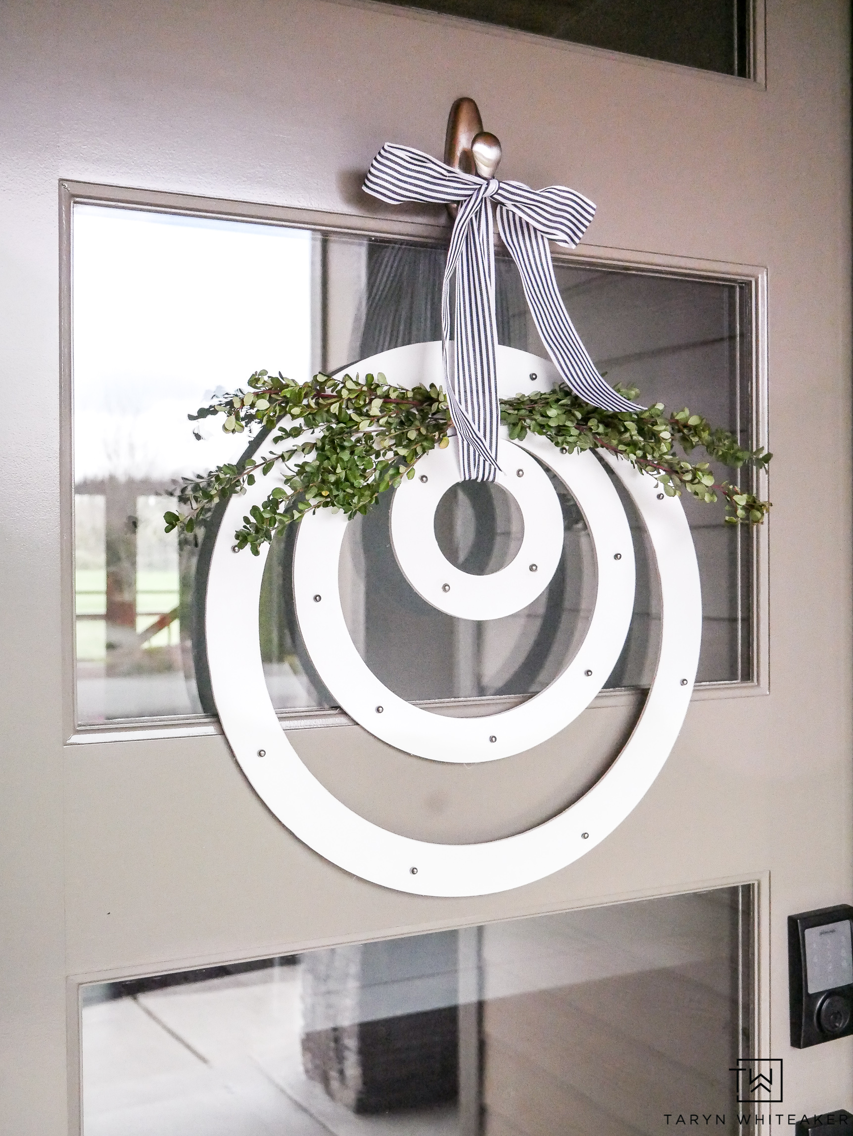 DIY Modern Spring Wreath. Three simple wood circles hung with branches and a striped ribbon hanging on a tan door.