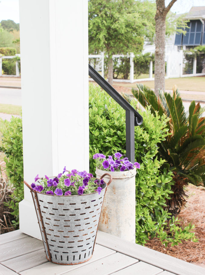 Purple pansies potted in reclaimed metal pots on a porch.