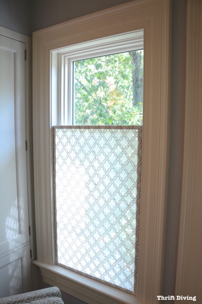 Opaque material wit a trellis patter is hung on the lower half of a window as a privacy screen that still lets light shine through.