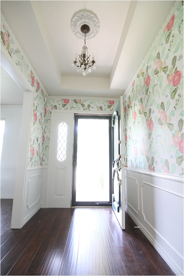Colorful pink flowers wit hgreen leaves are wallpaper that has been hung on the entryway of a home with white walls. 