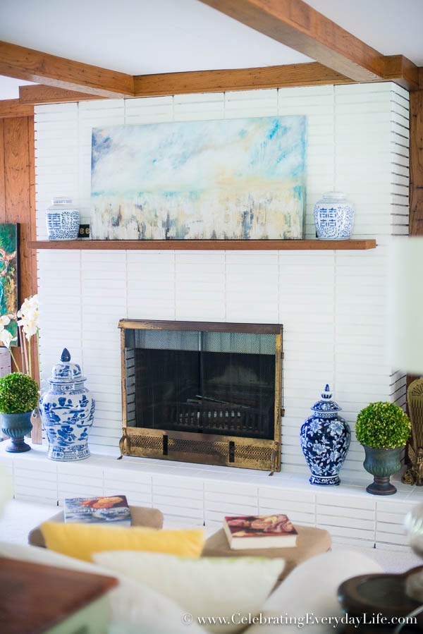 A brick fireplace has been painted white with a wood mantel and blue and white vases on the mantel and hearth.