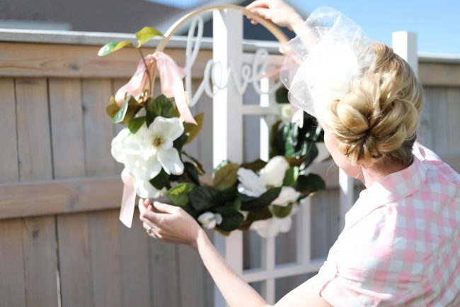 Making Your Wreath Once you have your materials, the steps are super easy: Align your garland along one side of your hoop. (Note: If you get your garland at Hobby Lobby, it'll come folded in half. I just use the entire thing, folded in half.) Use your wire or twine to affix your garland to the hoop. (I literally just wrap and wrap and wrap, and then tie it off at the end.) Now that your garland is affixed, place your metal word in the middle of the hoop wherever you like. Thread your twine or wire through your word, wrap it around the top of the hoop, and tie it off. (The word I found, "love," has little hooks on the back, so I just threaded the wire through those. If you have a word with no hooks, just thread it through the letters themselves.) Once your garland and word are affixed, select the ribbon you want to use to hang your wreath, and tie it at the top. Voila! You're done!