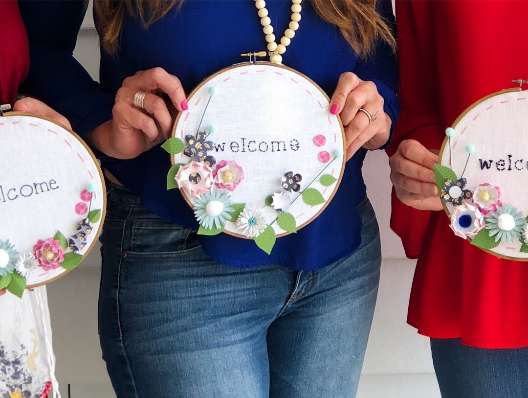 Make an embroidery hoop wall hanging. A hand-stitched word is surrounded by vibrant paper flowers in an embroidery hoop. Make one for your home or to give as a gift! 