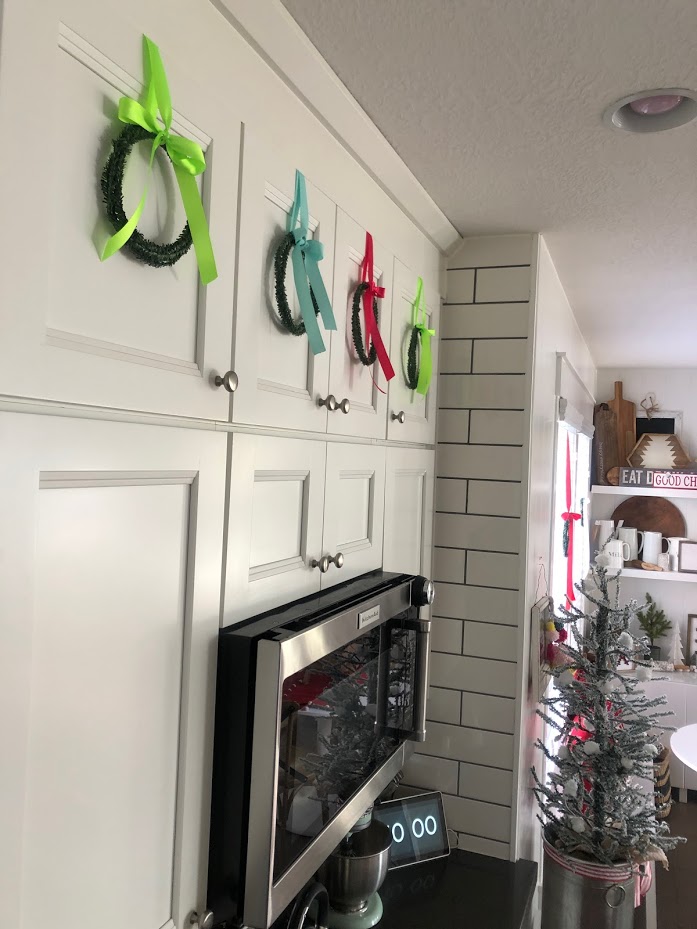 How to make mini cupboard wreaths for a dollar. Make mini wreaths out of tiny rolls of garland and hang them on your kitchen cupboards or on the back of chairs for the holidays. 