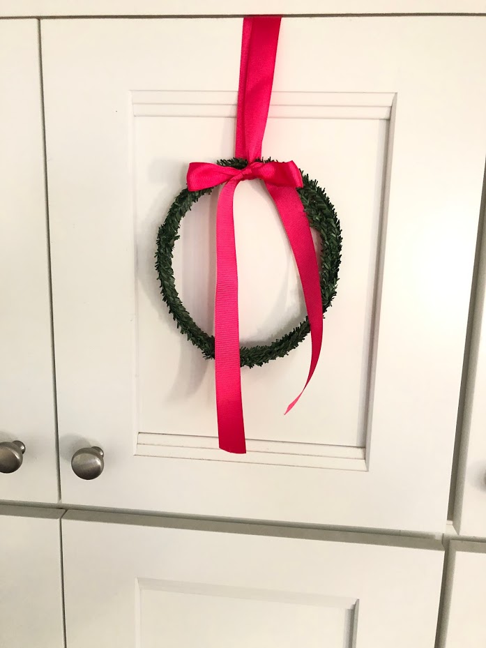 How to make mini cupboard wreaths for a dollar. Make mini wreaths out of tiny rolls of garland and hang them on your kitchen cupboards or on the back of chairs for the holidays. 