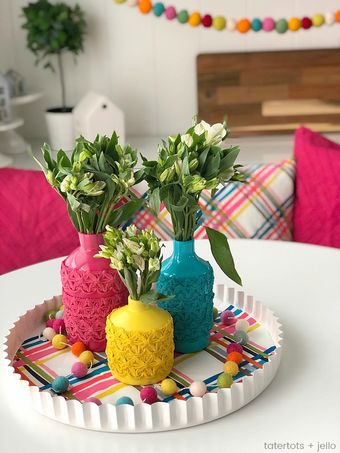 Anthropologie-Inspired Colorful Spring Vases DIY. Take simple jars, add spray paint and trim to create a beautiful centerpiece for a fraction of the cost! 