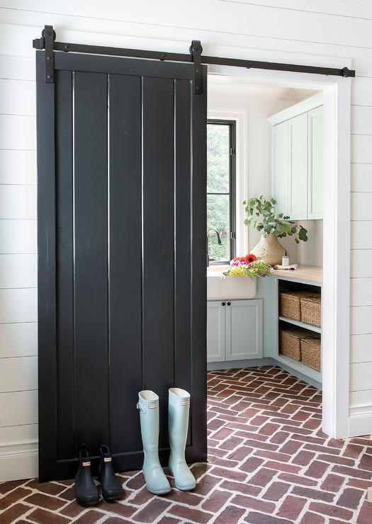 Red brick floor leading into laundry room with black barn door.