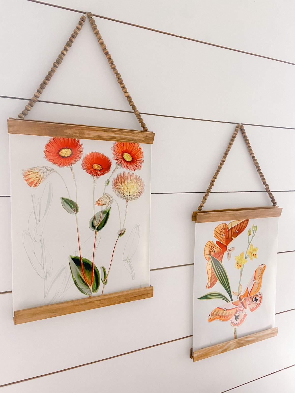 Vintage flowers and butterfly paintings hung on a wall with stained wood strips and beaded string.