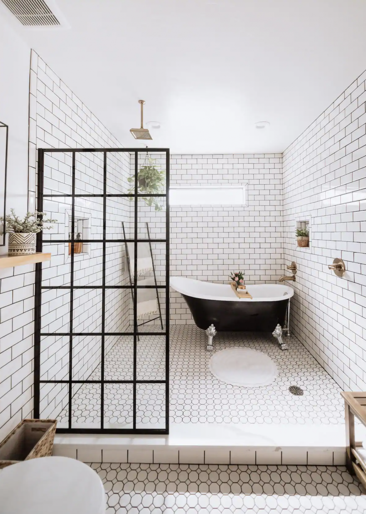 Black clawfoot tub in a shower wet room with subway tile and a glass grid panel. 