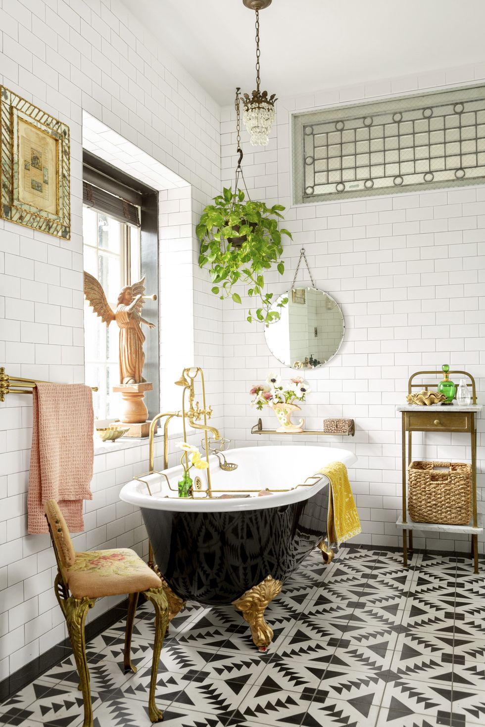 Black clawfoot tub and gold feet against a wall of subway tile and plants. 