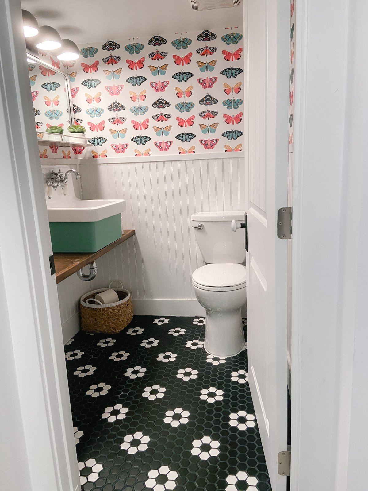 Butterfly wallpaper over beadboard wall with green sink and black and white hex tile. 