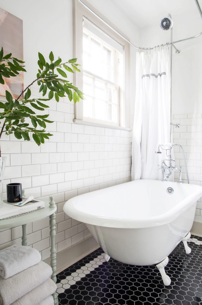 Black and white hex tile floor with white subway tile walls and a white clawfoot tub.