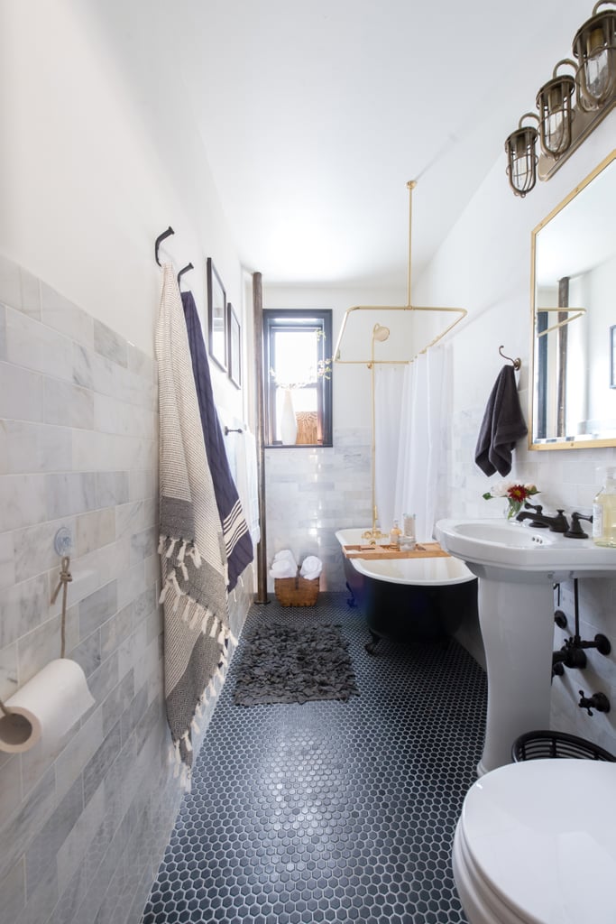 Black clawfoot tub with black penny tile floor, marble walls and brass fixtures. 