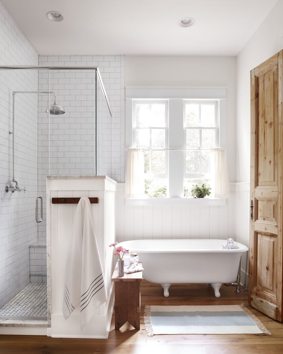 White small clawfoot tub in a bathroom next to a enclosed shower. 