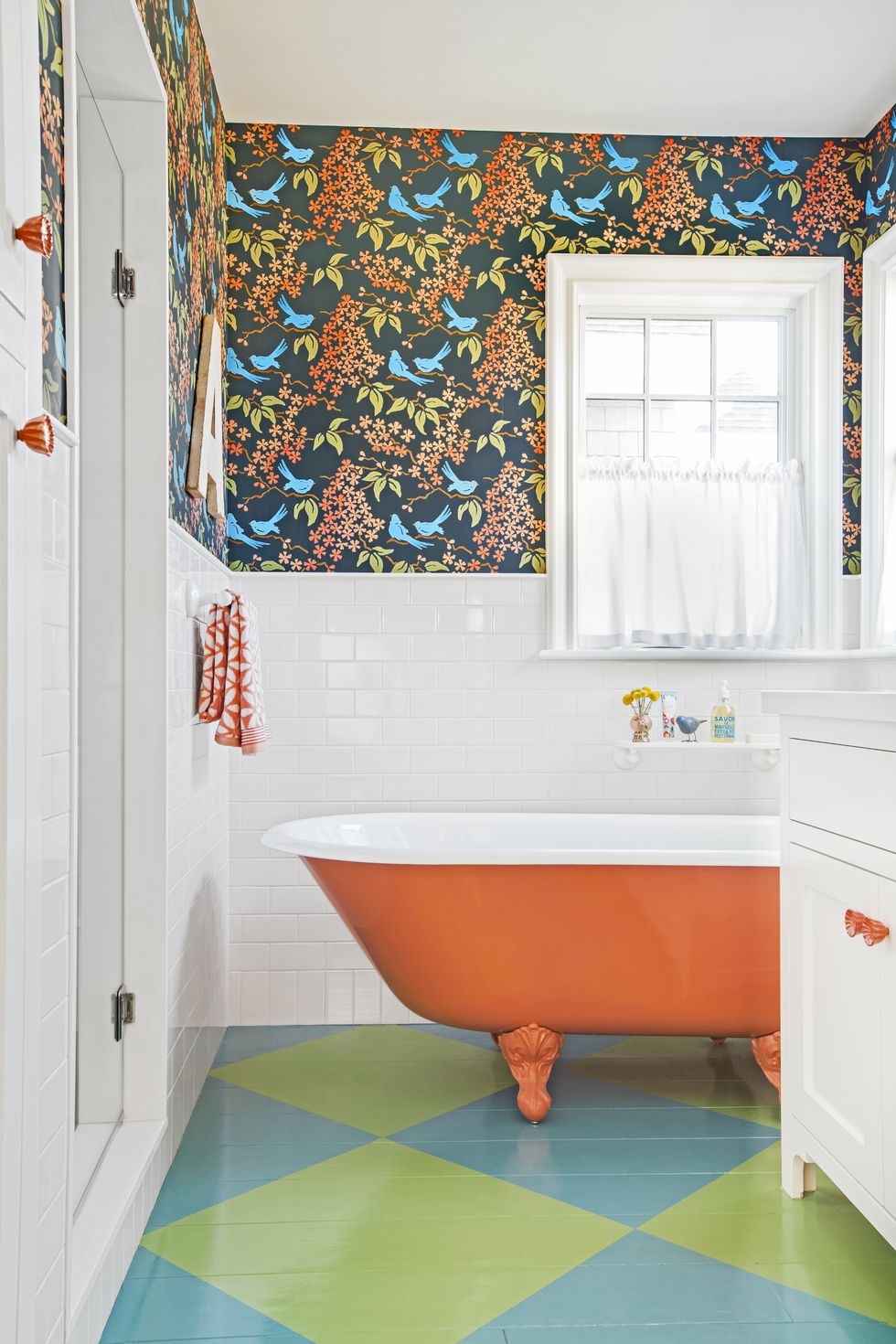 Orange clawfoot tub with painted bathroom floor and colorful wallpaper.