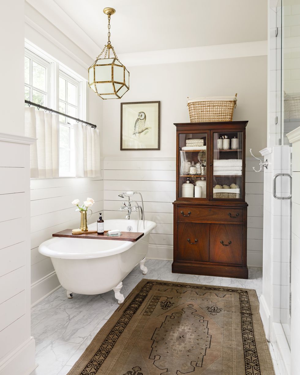 white clawfoot tub with shiplap walls. Traditional pendant light and antique cabinet for bathroom storage. 