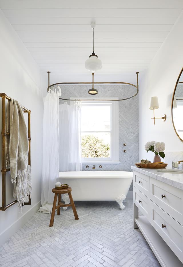 White clawfoot tub with marble herringbone tile walls and floor. Brass hardware 