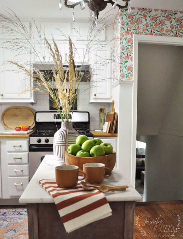 Green apples in a wood vase and dried grassesin a geometric vase on an island for early fall kitchen decor at Jennifer Rizzo. 