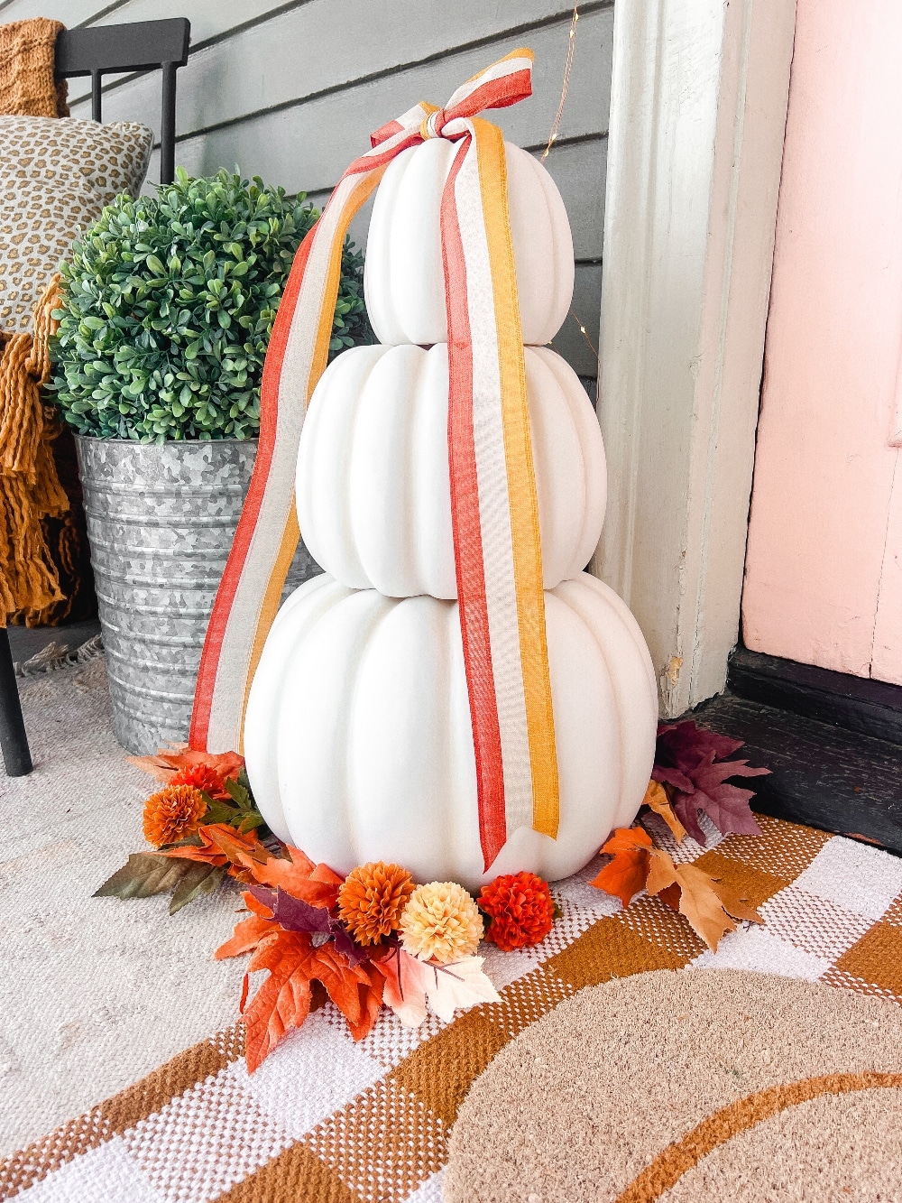 Candy Corn-Colored Fall Porch with Stacked Pumpkins. Create a warm, inviting fall porch with the coolest stacked pumpkins, a vibrant DIY wreath, and layered plaid rugs for a festive, seasonal touch.