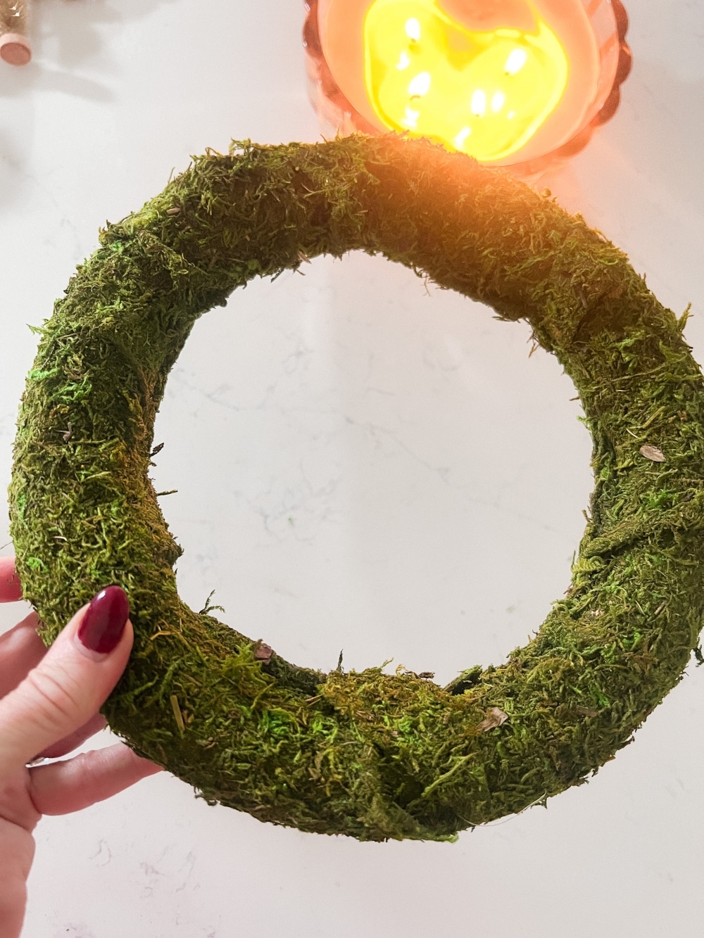 Cozy Dollar Store Christmas Centerpiece. Create a Terrain-inspired holiday centerpiece on a budget with dollar store finds! This DIY project combines bottle brush trees and a moss-covered wreath form, giving a high-end look without breaking the bank. Battery operated lights glow along with a candle in the center for a cozy addition to the holiday season.