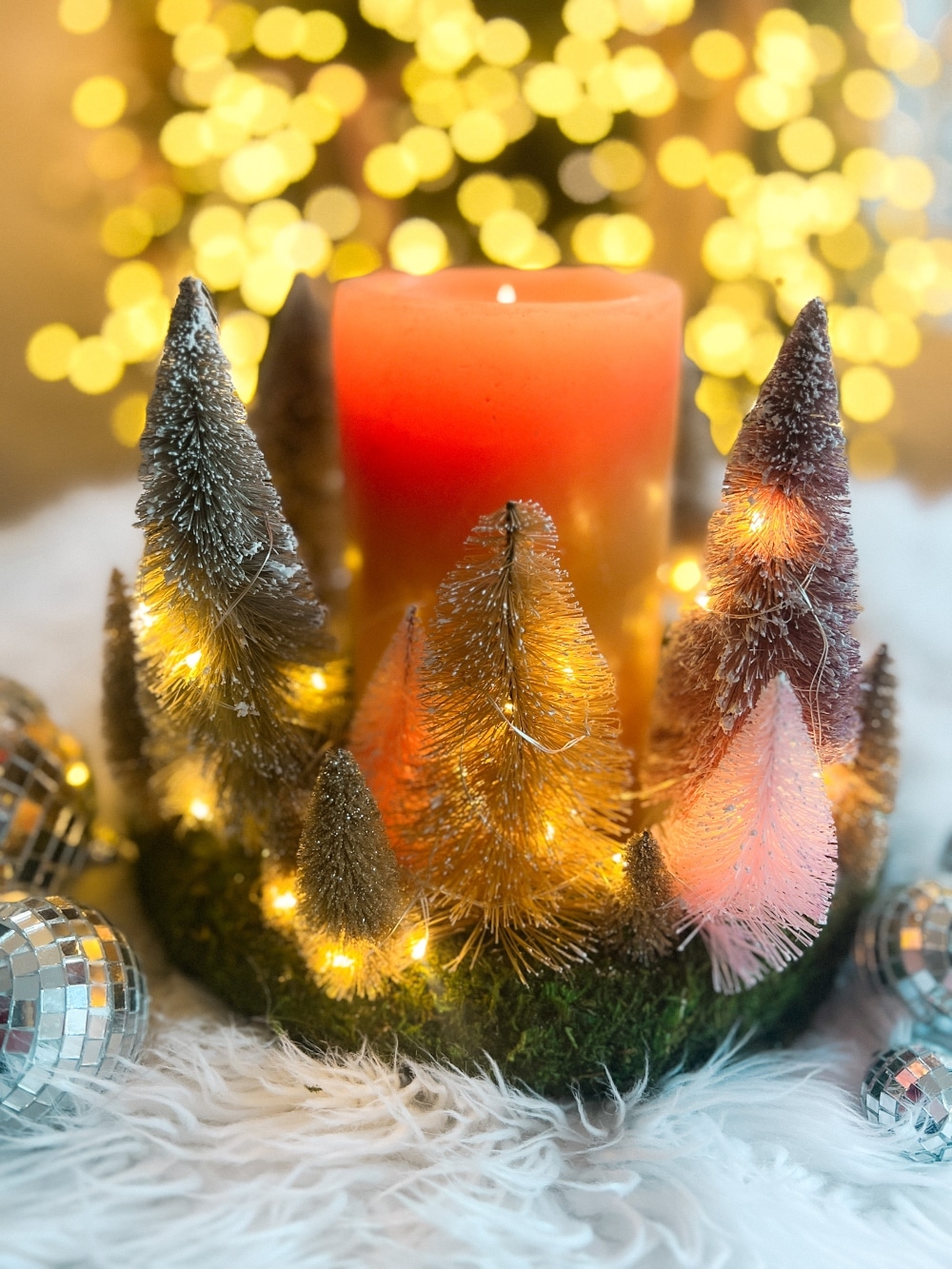 Cozy Dollar Store Christmas Centerpiece. Create a Terrain-inspired holiday centerpiece on a budget with dollar store finds! This DIY project combines bottle brush trees and a moss-covered wreath form, giving a high-end look without breaking the bank. Battery operated lights glow along with a candle in the center for a cozy addition to the holiday season.