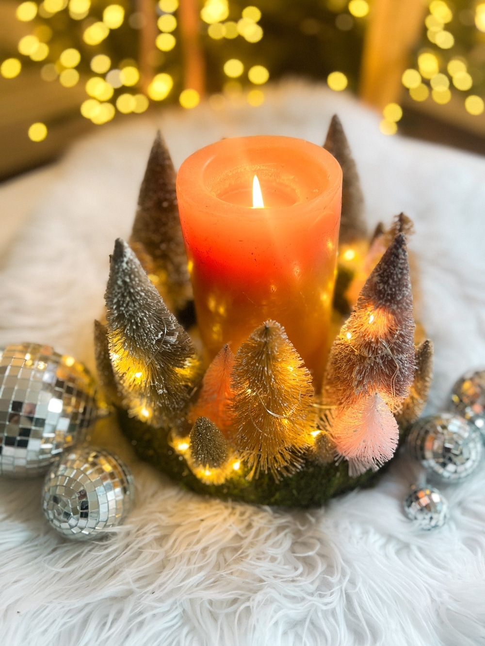 Cozy Dollar Store Christmas Centerpiece. Create a Terrain-inspired holiday centerpiece on a budget with dollar store finds! This DIY project combines bottle brush trees and a moss-covered wreath form, giving a high-end look without breaking the bank. Battery operated lights glow along with a candle in the center for a cozy addition to the holiday season.