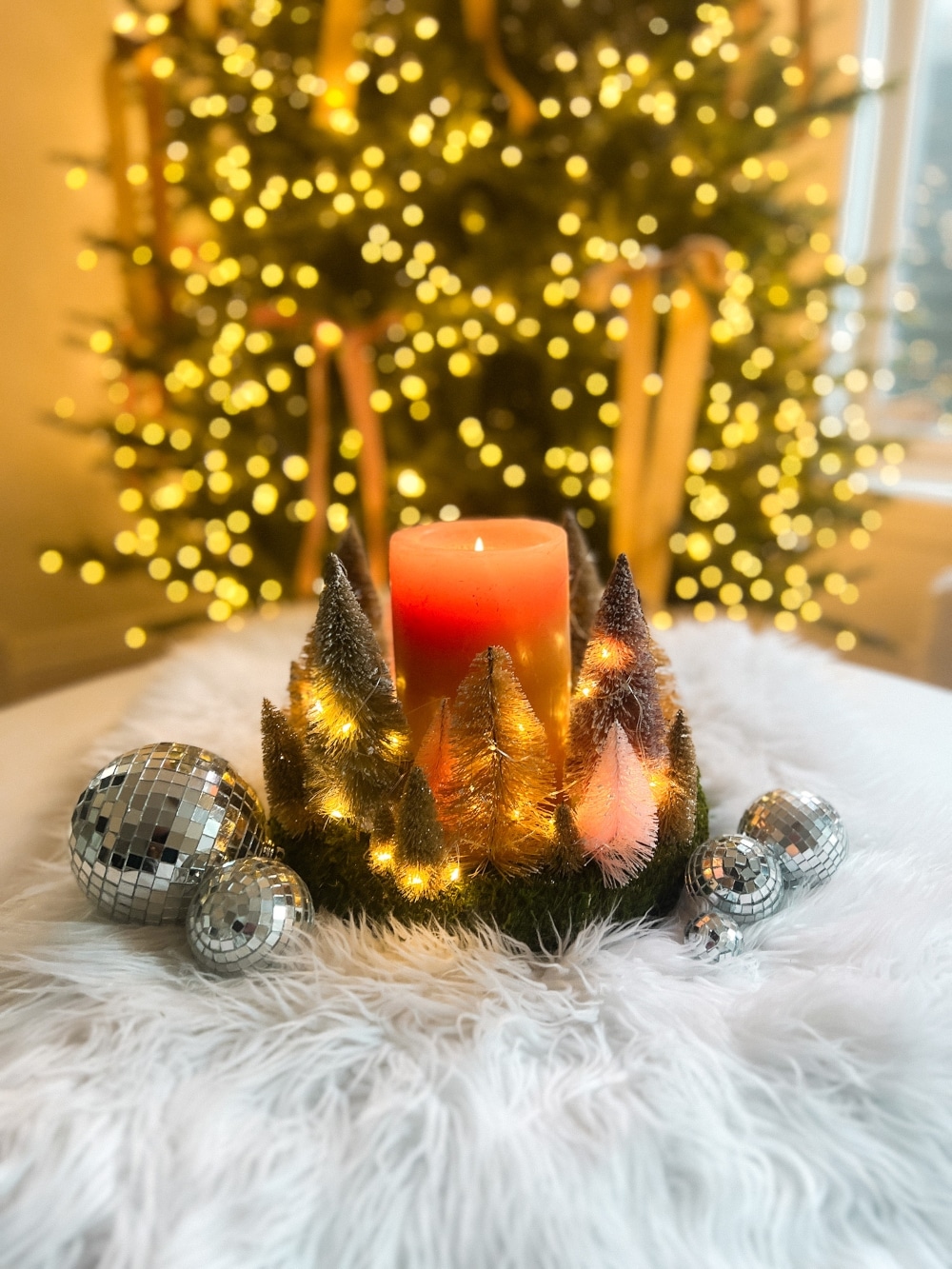 Cozy Dollar Store Christmas Centerpiece. Create a Terrain-inspired holiday centerpiece on a budget with dollar store finds! This DIY project combines bottle brush trees and a moss-covered wreath form, giving a high-end look without breaking the bank. Battery operated lights glow along with a candle in the center for a cozy addition to the holiday season.