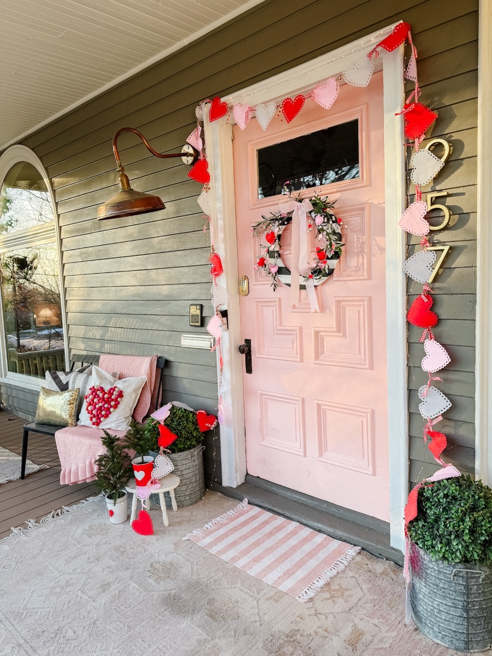 A Festive and Cozy Valentine’s Day Porch. A DIY Valentine’s porch with a striped heart wreath, felt banners, cozy pillows, and festive decor.