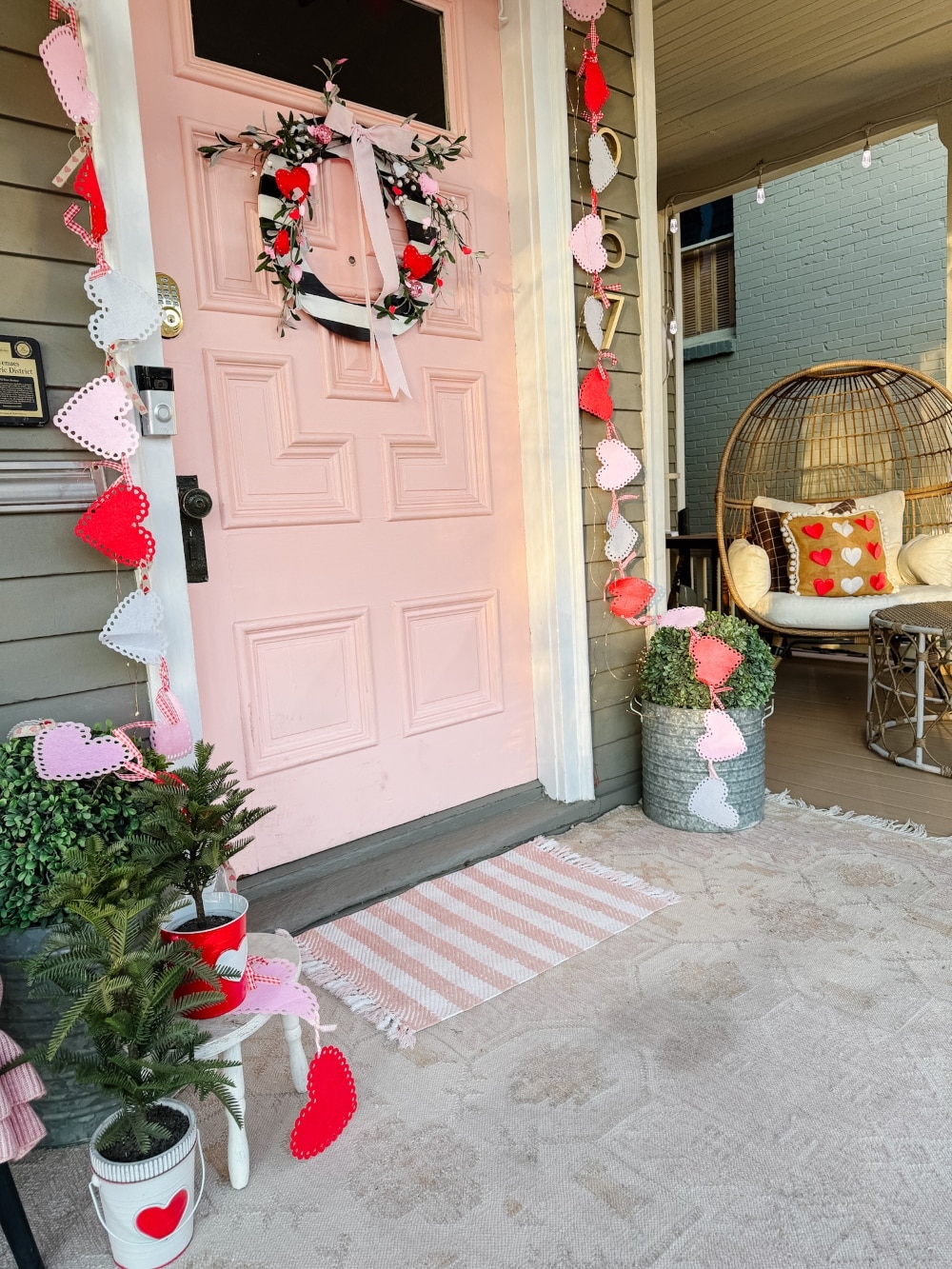 A Festive and Cozy Valentine’s Day Porch. A DIY Valentine’s porch with a striped heart wreath, felt banners, cozy pillows, and festive decor.